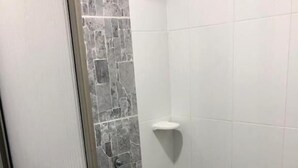 A shower with a stone wall and white tiles.