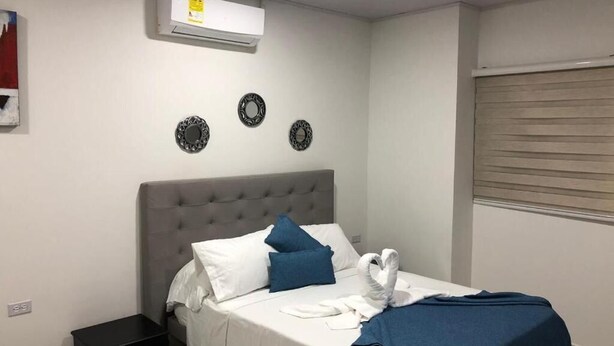 A neatly made bed with white and blue bedding, a grey headboard, and a wall-mounted air conditioner.