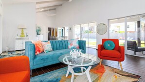 Un salón espacioso con un sofá azul, un sillón rojo, una mesa de centro de cristal y una alfombra colorida.