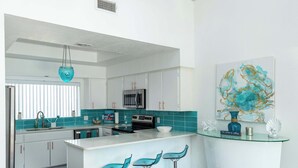 Una cocina moderna con armarios blancos, una isla central con taburetes de bar, un microondas y un lavabo con grifo.