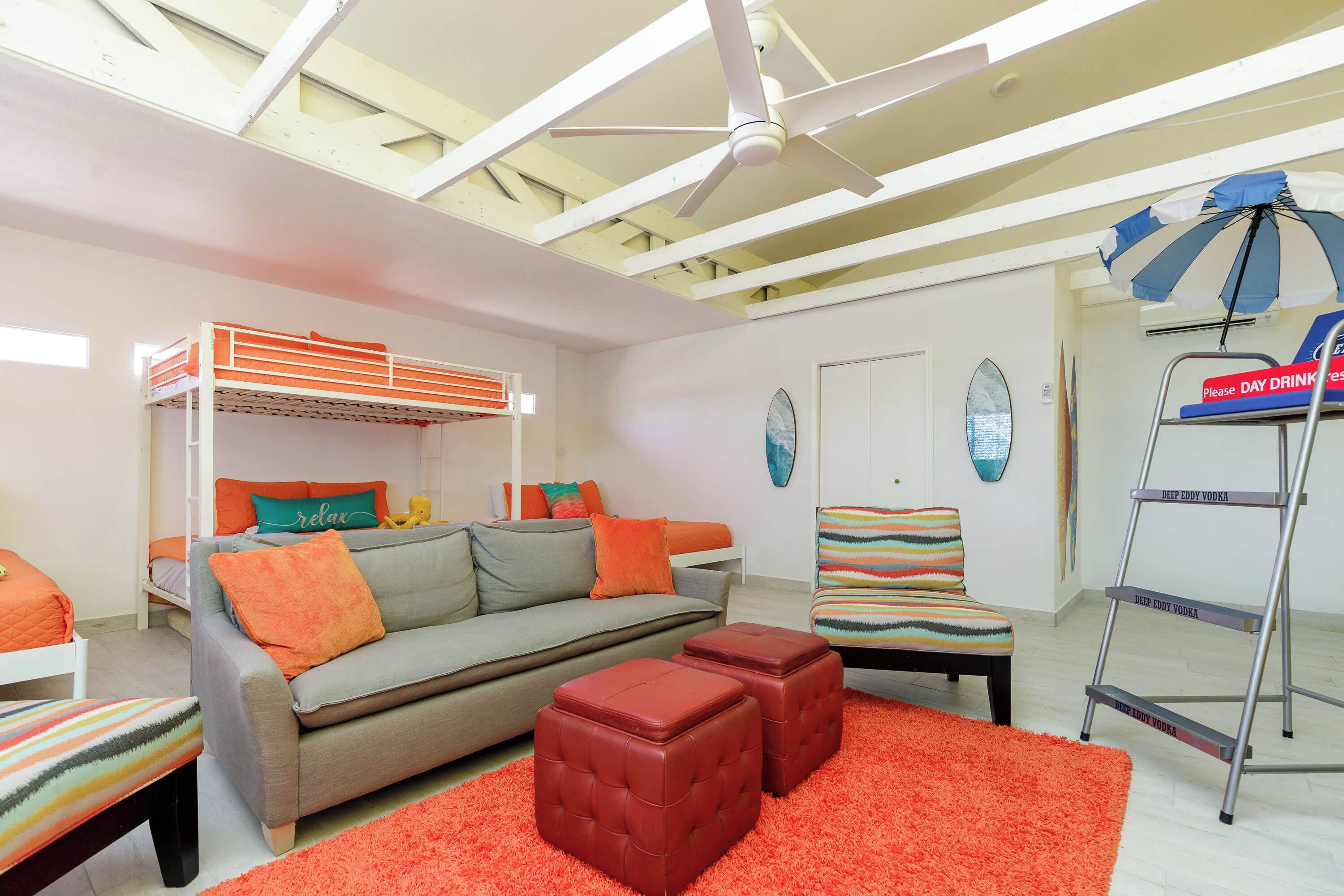 A modern living room with a sofa, ottomans, a bunk bed, a colorful chair, and a ladder.