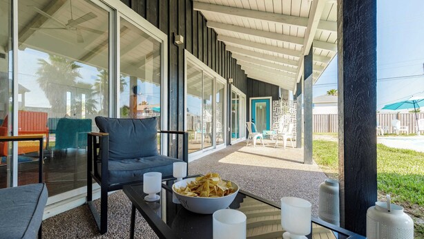 Un área de estar al aire libre con techo, una mesa de vidrio, sillas y un bol de papas fritas.