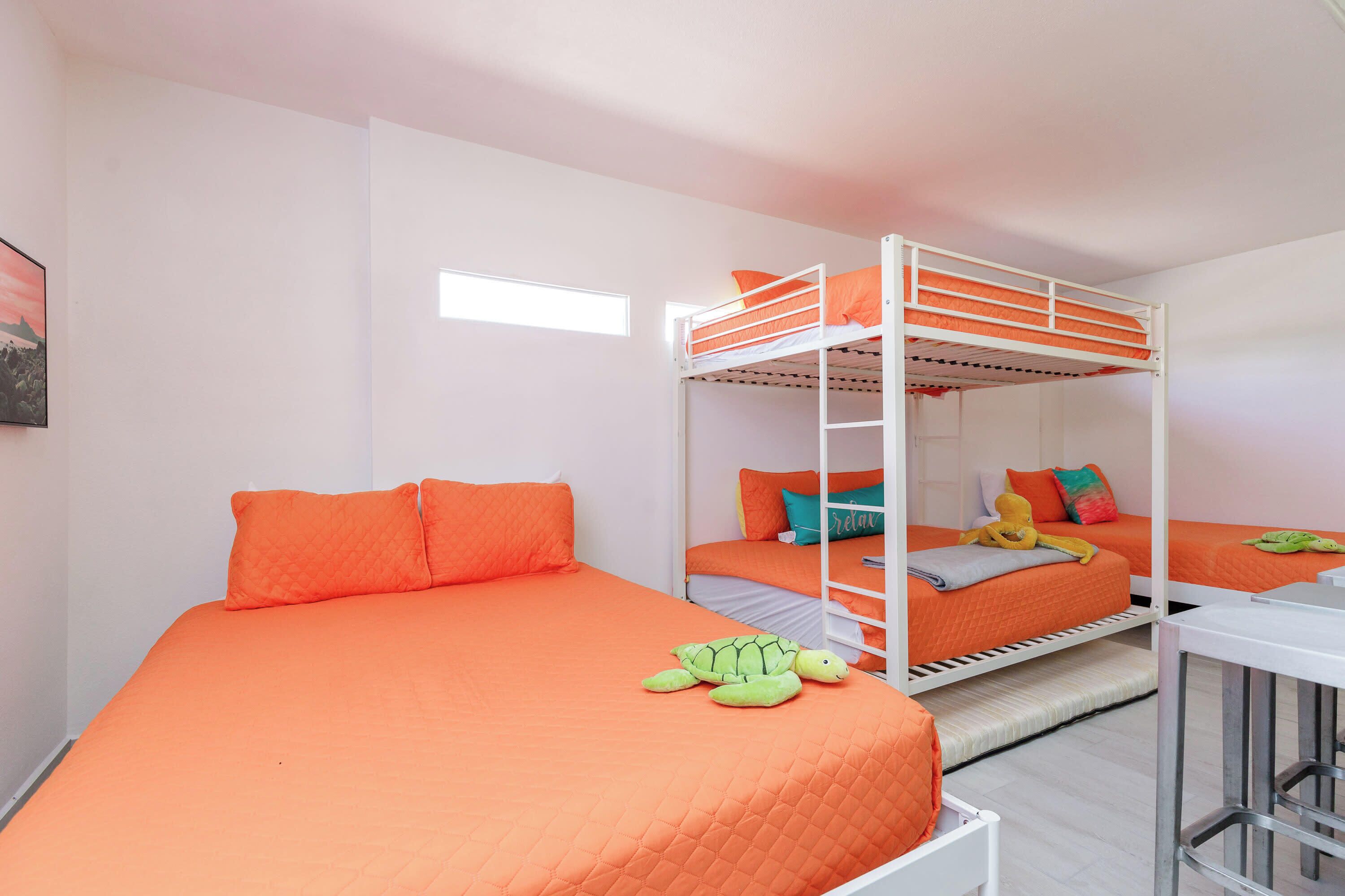 Ein Zimmer mit drei Etagenbetten, jeweils mit orangefarbener Bettwäsche und Kissen. In der Ecke steht ein kleiner Tisch und ein Stuhl.