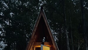 A wooden A-frame cabin with a bed inside, a welcome sign, and a small porch area with lights. - Lakefront Transforming Micro Cottage on Cherokee Lake  (Mooresburg)
