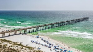 A beach with a long pier extending into the ocean, sandy beach, and umbrellas.