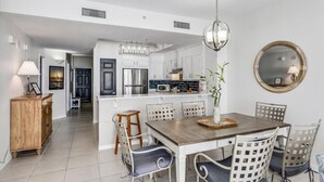 A modern kitchen with white cabinetry, a central island, and a dining area with a wooden table and white chairs.