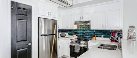 A modern kitchen with white cabinetry, stainless steel appliances, a black door, and a teal backsplash.
