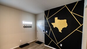 En hall med en svart vägg som har en guldkantad avbildning av delstaten Texas, en vit dörr och en svart matta på golvet.