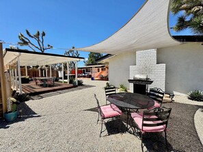 An outdoor patio area with a round table and chairs, a barbecue grill, and a covered seating area. - Mid-Century • Pool & Spa • Games • Near JTree Park (Yucca Valley)
