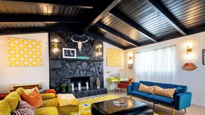 Ein modernes Wohnzimmer mit Kamin aus Stein, einem blauen Sofa, gelb-orangen Kissen und geometrischen Wandmustern.