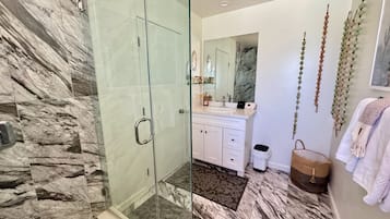 A modern bathroom with a glass shower enclosure, marble flooring, a white vanity with a mirror, and a hanging plant.