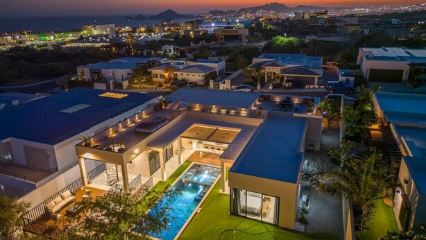 Un complejo residencial moderno con varios edificios, una piscina y vistas de la ciudad al anochecer.