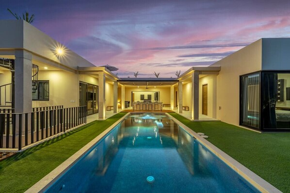 Ein modernes Haus mit Swimmingpool, Bar und gut beleuchtetem Innenraum.