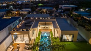 Una casa moderna con piscina, mobiliario exterior y vistas a la ciudad al atardecer.
