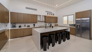 Una cocina moderna con armarios de madera, una isla central con taburetes, un refrigerador de acero inoxidable e iluminación colgante.