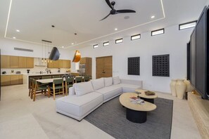 A modern living room with a sectional sofa, a dining area with chairs, a ceiling fan, recessed lighting, and a large window. - Casa Herradura - Ocean View Luxury Villa (Cabo San Lucas)