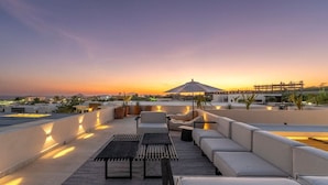 Una terraza en la azotea con asientos, una mesa y vistas al atardecer.
