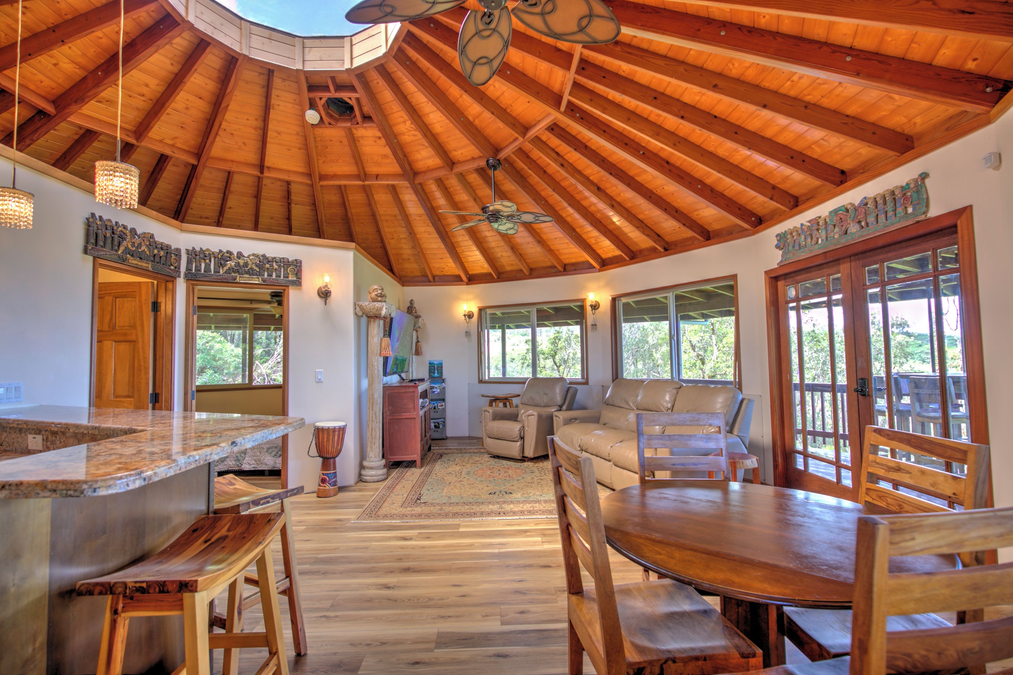 A spacious interior with a high wooden ceiling, a dining area with wooden furniture, and a view through large windows.