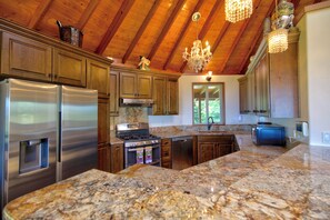 Cocina con encimeras de granito, electrodomésticos de acero inoxidable, armarios de madera y una araña.