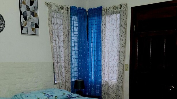 A room with a bed, a window with curtains, a door, and a wall decoration. - Hospedaje Casa de Luna (Tegucigalpa)