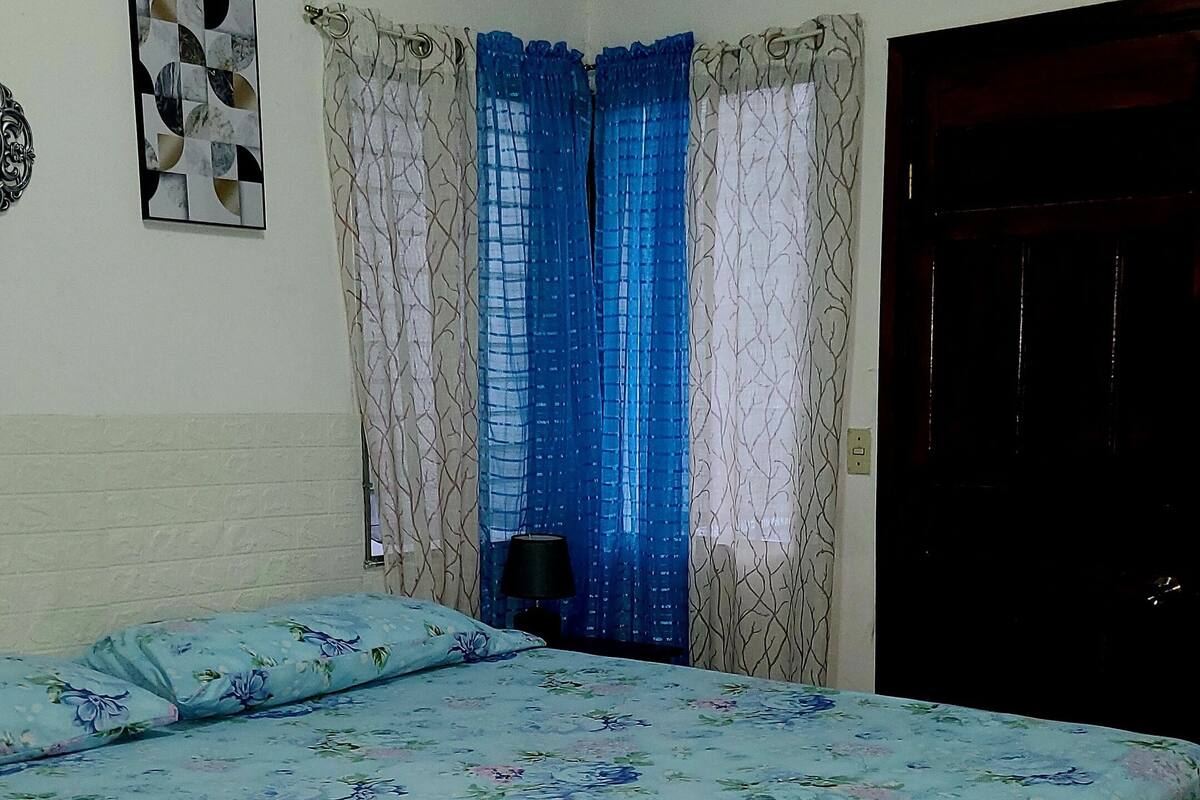 Une pièce comprenant un lit, une fenêtre avec des rideaux, une porte et un élément décoratif mural.