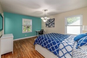A bedroom with teal walls, a wooden floor, a bed with a blue and white patterned bedspread, a desk, and a chair. - Centrally Located Spacious Abode (Charlotte)