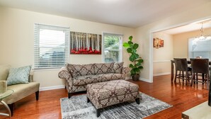 Ein Wohnzimmer mit einer Couch, einem Hocker und einem Essbereich mit Tisch und Stühlen.