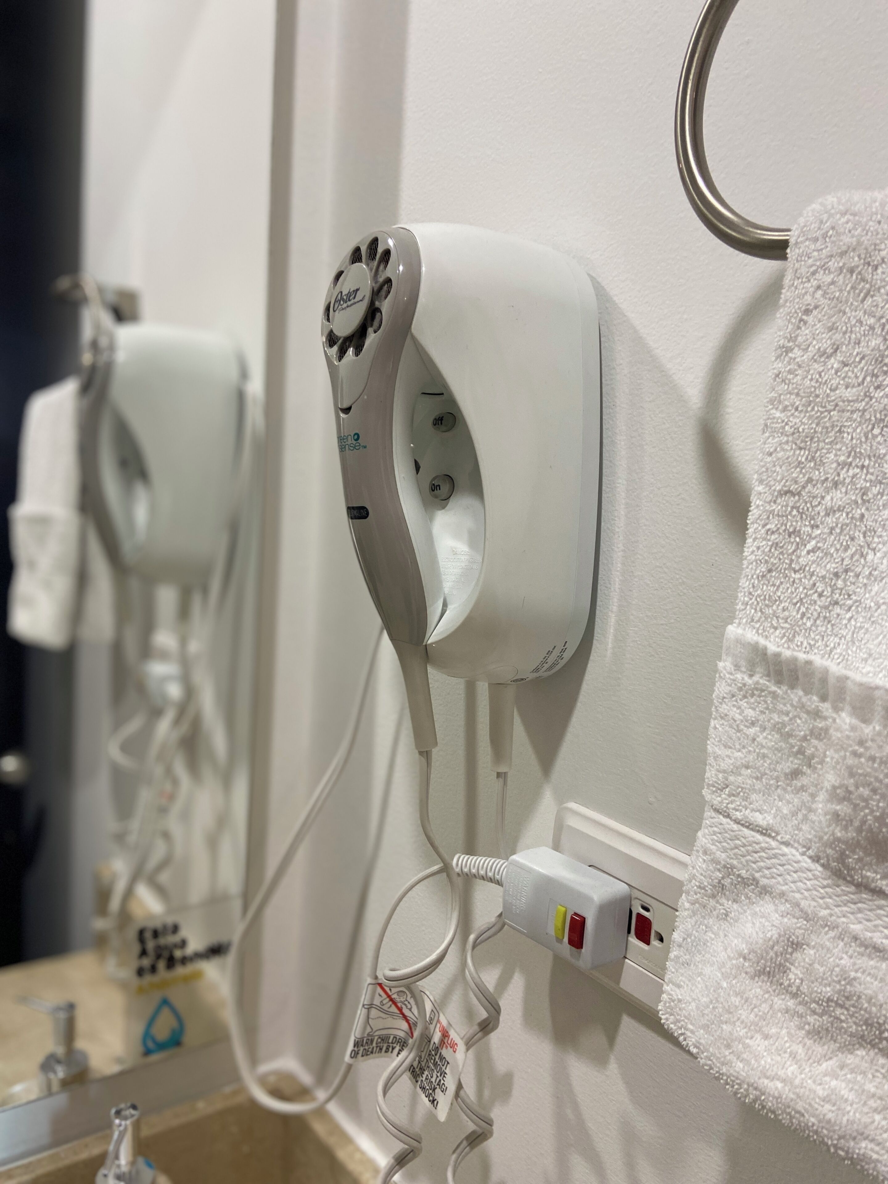 A hairdryer mounted on a wall with a towel hanging nearby.