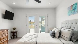 Een slaapkamer met een groot bed, een plafondventilator, een flatscreen-tv en een schuifdeur naar buiten.