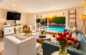 A living room with a pool view, a flat-screen TV, and a sofa with a vase of red tulips.
