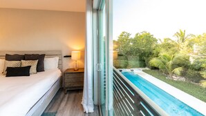 A bedroom with a large bed, a bedside table with a lamp, and a view of a swimming pool and greenery outside. - 30% Off September! Walk To Beach/Pool-CV41-2 (Leeward Settlement)