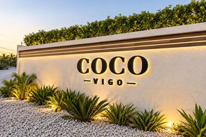 A sign with the name 'COCO VIGO' illuminated against a wall, surrounded by plants and gravel. - Walk 2 Beach, Pool, Private Patio & Balcony-CV41-2 (Leeward Settlement)