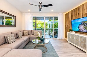 A modern living room with a sectional sofa, a glass coffee table, a ceiling fan, and a TV on a wooden cabinet. - Walk 2 Beach, Pool, Private Patio & Balcony-CV41-2 (Leeward Settlement)