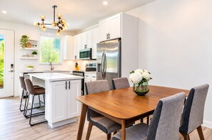 Une cuisine moderne avec des meubles blancs, un réfrigérateur en acier inoxydable et un coin repas comprenant une table en bois et des chaises à revêtement gris.