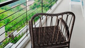 Un balcon avec un fauteuil en osier, une balustrade et une vue sur un paysage montagneux.