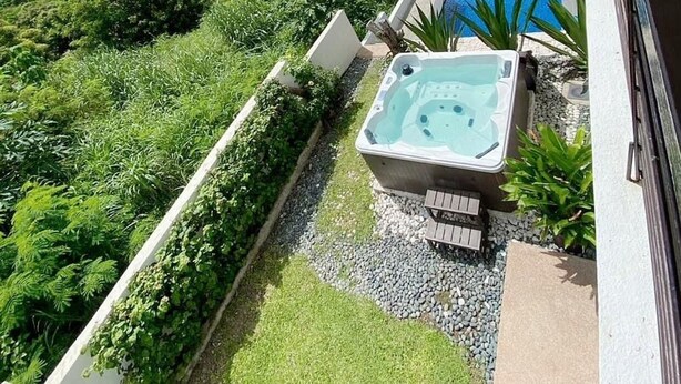 Un bain à remous et une piscine sur un balcon offrant une vue sur un lac et des collines.
