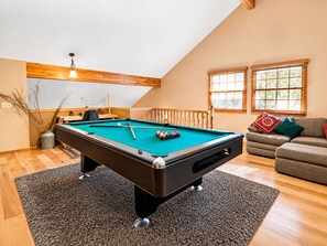 A pool table in a room with a sloped ceiling, a wooden railing, and a sofa with cushions.