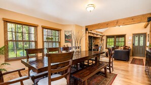 A dining area with a wooden table and chairs, a rug, and a view of the outdoors through large windows.