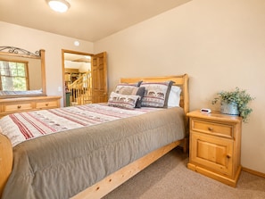 A bedroom with a bed, wooden nightstands, a dresser, a mirror, and a door leading to a hallway.
