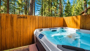 A hot tub in a wooden deck area with a wooden fence labeled 'Towels' and a forest background.