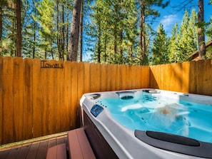 A hot tub in a wooden deck area with a wooden fence labeled 'Towels' and a forest background.