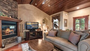 A cozy living room with a fireplace, a television, a sofa, and a coffee table. - Big Bear Villa - Walk to Lake & Village, Hot Tub, Jet Tub, Outdoor Shower (Big Bear Lake)