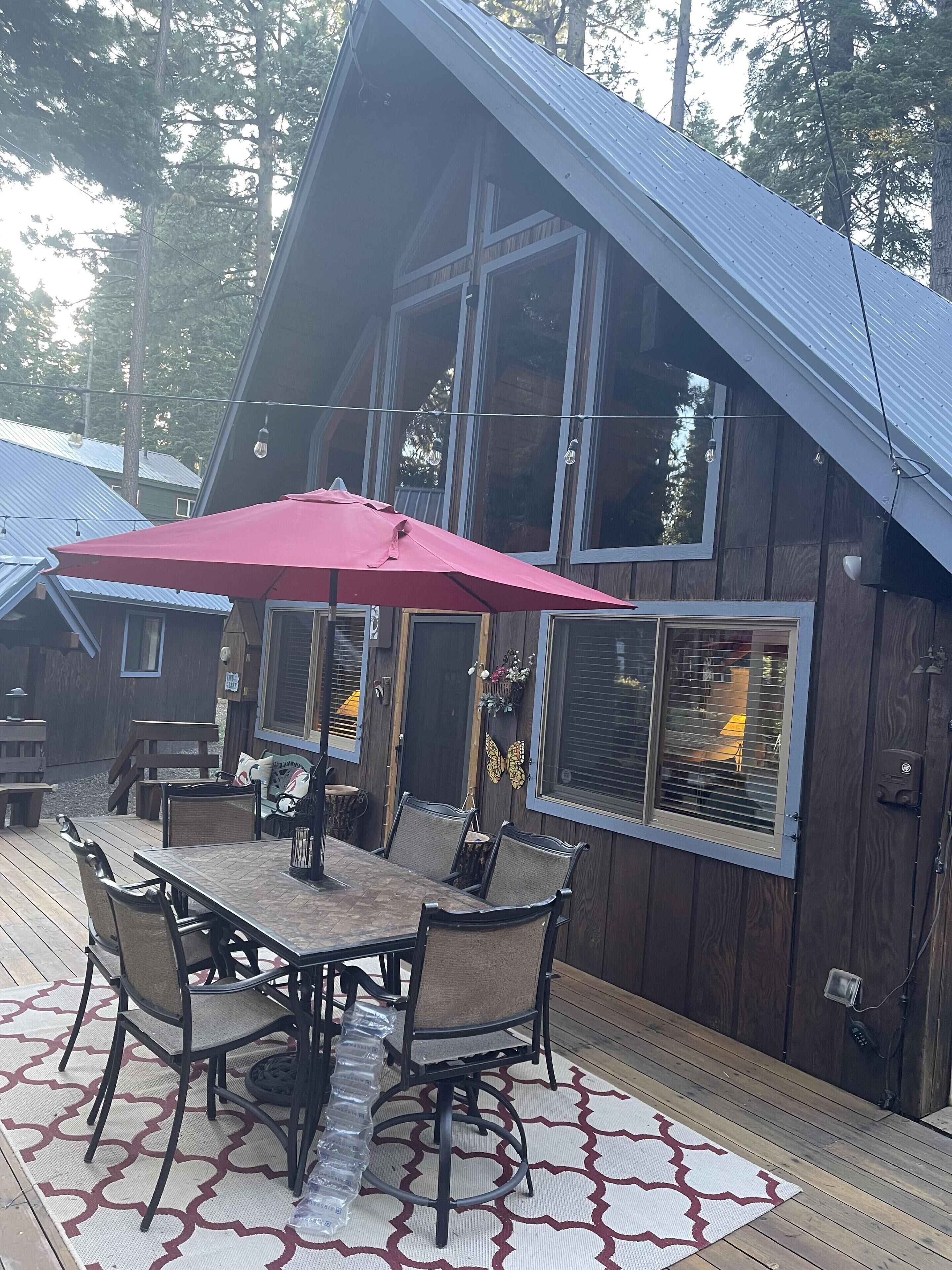 A wooden cabin with a deck, a dining table with chairs, and a red umbrella.
