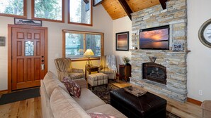 A cozy living room with a stone fireplace, wooden ceiling beams, a large window, and a comfortable seating area. - Inviting and Modern Home in Sunnyside Walk to Lake, Access to Tahoe Park HOA.  By Tahoe Time VR (Tahoe City)