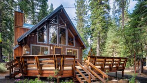A wooden cabin with a steeply pitched roof, large windows, and a wooden deck with stairs leading to the entrance. - Inviting and Modern Home in Sunnyside Walk to Lake, Access to Tahoe Park HOA.  By Tahoe Time VR (Tahoe City)