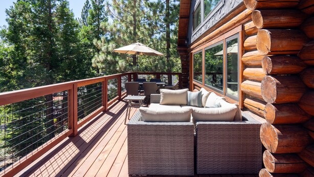 A log cabin with a deck featuring wicker furniture and a table with chairs.