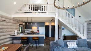 A spacious living area with a grey sofa, a wooden dining table, and a kitchen in the background.