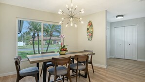 A dining area with a table, chairs, a chandelier, a window with a view of palm trees, and a door. - Poolside Oasis - Modern spacious 3 bedroom, 2 bathroom private pool home in Sarasota near Siesta Key (Sarasota)