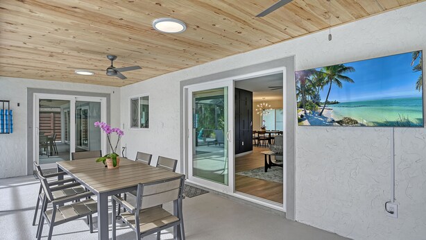 A modern dining area with a wooden table and chairs, a ceiling fan, and a view of the outdoors through glass doors. - Poolside Oasis - Modern spacious 3 bedroom, 2 bathroom private pool home in Sarasota near Siesta Key (Sarasota)