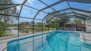 An indoor swimming pool with clear views of the surrounding landscape, including a lake and houses.